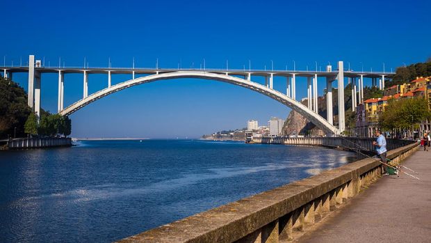 Jembatan Arrabida di Porto, Portugal Porto, Portugal - May, 2018: Man fishing close to the Douro River mouth and the Arrabida Bridge in a beautiful early spring day at Porto City in Portugal