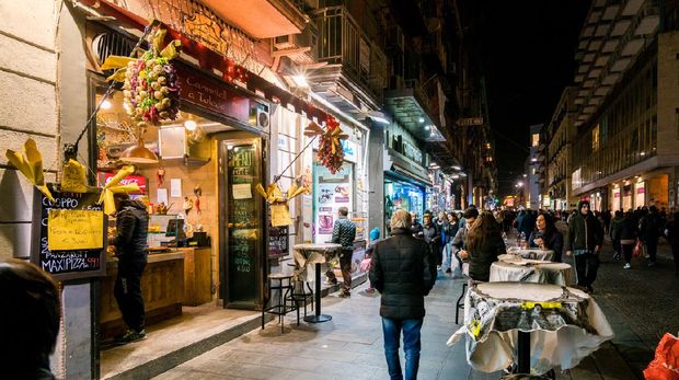 Naples, Italy - February 25, 2016: View of Via Toledo in Naples, Italy at night with people walking around. Restaurant Carmniell a Toledo can be seen in the foreground.
