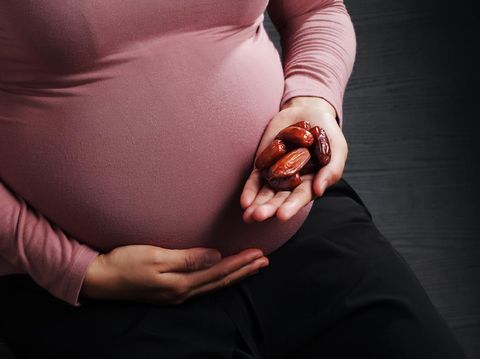 Pregnant woman holding dried Date Palm fruit on black background