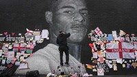 Seorang seniman yang dikenal sebagai AKSE-P19 tengah memperbaiki mural pesepakbola Marcus Rashford yang sebelumnya menjadi sasaran vandalisme dan serangan rasial.