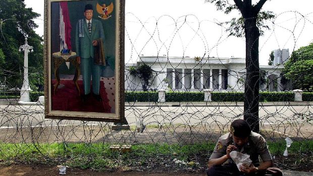 A lone Indonesian policeman takes a lunch at a street-stall with portrait of ousted president Abdurrahman Wahid displayed on a barbed wire used as a barricade outside the presidential palace, 24 July 2001, a day after the national assembly dismissed the 60-year old liberal democrat president  out of power.  The road to the palace remain deserted as Jakarta's elite abandoned the former president.  AFP  PHOTO (Photo by CHOO YOUN-KONG / AFP)