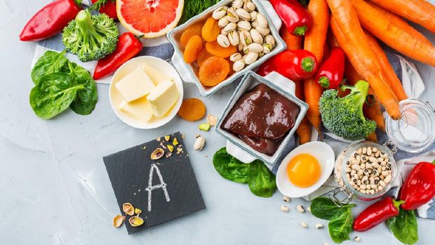 Assortment of high vitamin A sources on dark background: butter, avocado, dried apricots, eggs, paprika, liver, spinach, apples, tomatoes, milk, cheese. Top view.