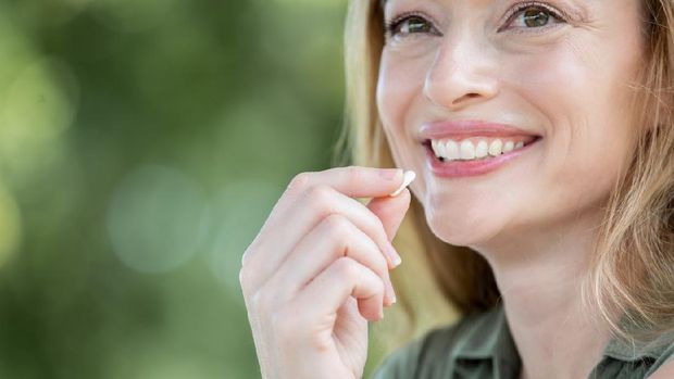 Smiling woman holds vitamin up to mouth