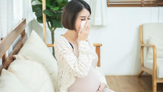 pregnant asian female use tissue paper close mouth and nose, she cough and feeling fever, pregnancy and people concept - sick pregnant woman blowing nose with paper tissue at home