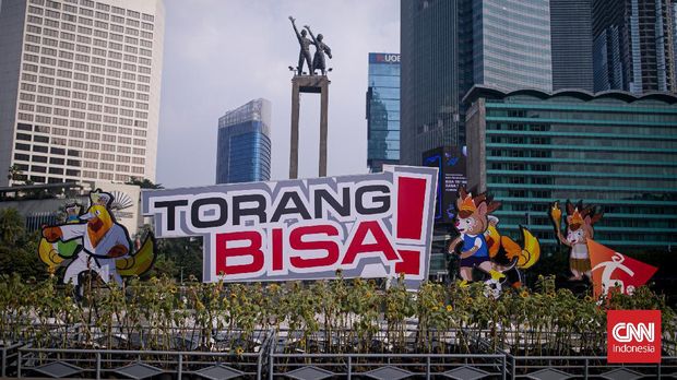 Pengendara sepeda motor melintas di dekat maskot dan slogan Pekan Olahraga Nasional (PON) XX Papua di Bundaran Hotel Indonesia, Jakarta, Jumat (16/7/2021). Presiden Joko Widodo memastikan PON XX Papua tetap akan berlangsung pada 2-15 Oktober 2021. CNNIndonesia/Adi Maulana Ibrahim