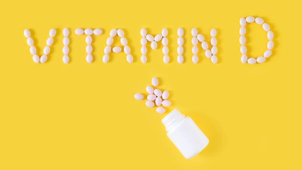 Vitamin D pills dropped from bottle on yellow background. Flat lay, top view, free copy space.