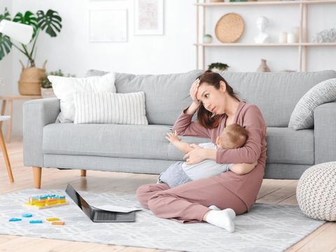 Motherhood Exhaustion Concept. Tired young mom breastfeeding baby and working on laptop at home, feeling frustrated, free space