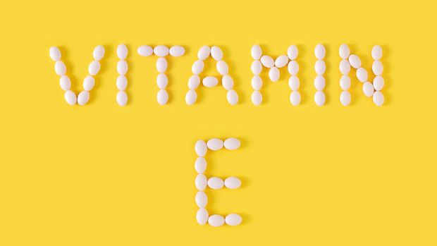 Vitamin E pills dropped from bottle on yellow background. Flat lay, top view, free copy space.