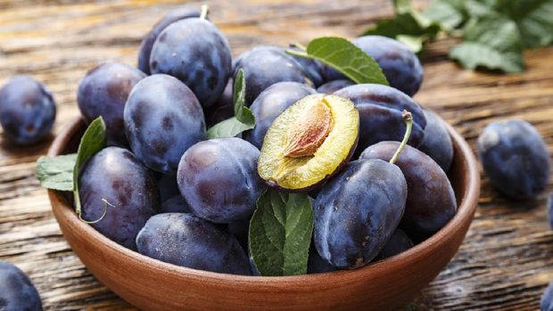 raw plums in a plate on a brown wooden background. place for text