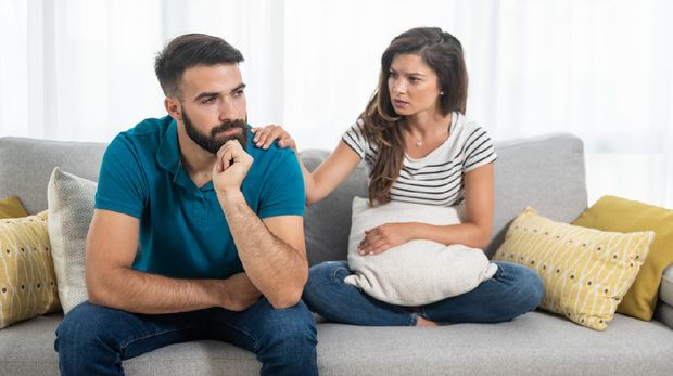 Young couple woman and man sitting on the sofa in the living room had an argue and not talking where girlfriend put her hand on the boyfriend shoulder and try to calm him down, relationship issues