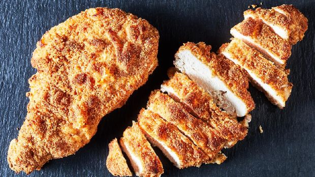fried breaded chicken breasts, a whole one and a sliced one on a black stone plate, horizontal view from above