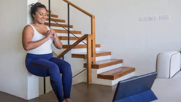 Ilustrasi olahraga panggul Portrait shot of an attractive Malaysian woman doing wall sit exercise in her living room during Covid 19 pandemic