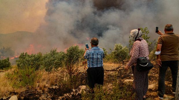 People take pictures with their phones during a massive forest fire which  engulfed a Mediterranean resort region on Turkey's southern coast near the town of Manavgat, on July 29, 2021. - At least three people were reported dead on July 29, 2021 and more than 100 injured as firefighters battled blazes engulfing a Mediterranean resort region on Turkey's southern coast. Officials also launched an investigation into suspicions that the fires that broke out Wednesday in four locations to the east of the tourist hotspot Antalya were the result of arson. (Photo by Ilyas AKENGIN / AFP)