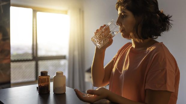 ilustrasi minum vitamin , vitamin Shot of a young woman taking supplements at home