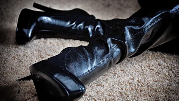 A pair of high heeled black leather boots on carpet.