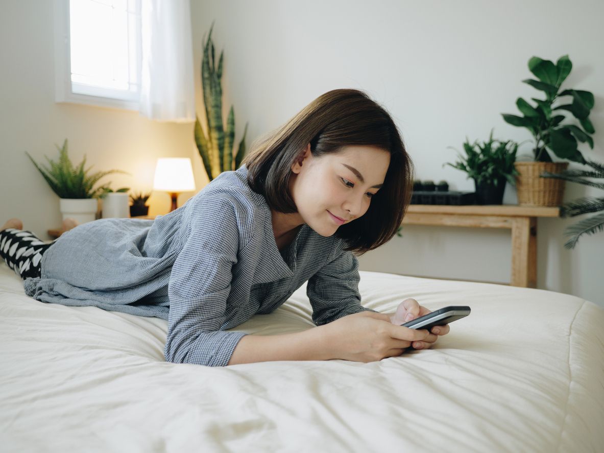 Young Asian woman using smart phone in bedroom happy and smile.