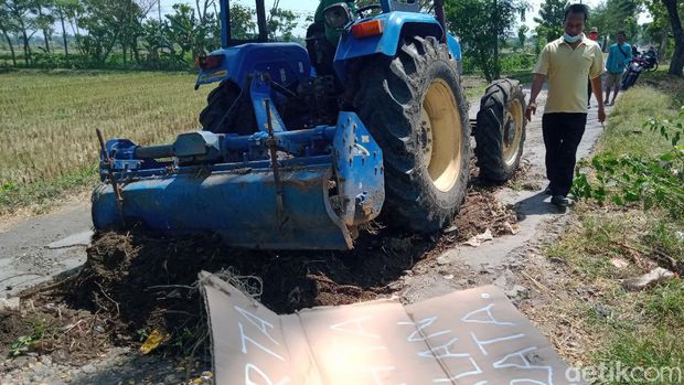 Kuburan di tengah jalan berbatu yang viral diuruk dengan alat berat. Ada poster tertulis, 'Harta, Tahta, Jalan Rata' di lokasi tersebut.