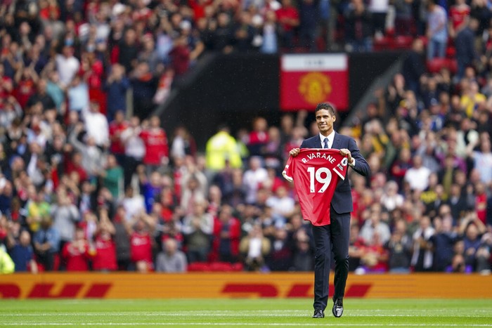 Raphael Varane Raphael Varane shows his shirt to the fans after signing for Manchester United ahead of the English Premier League soccer match between Manchester United and Leeds United at Old Trafford in Manchester, England, Saturday, Aug. 14, 2021. (AP Photo/Jon Super)