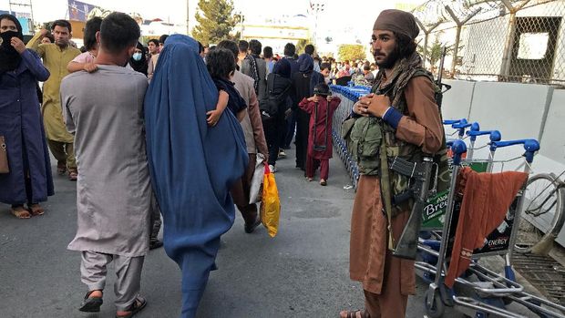 A member of Taliban stands guard as people walk at the entrance gate of Hamid Karzai International Airport in Kabul, Afghanistan, August 16, 2021.REUTERS/Stringer