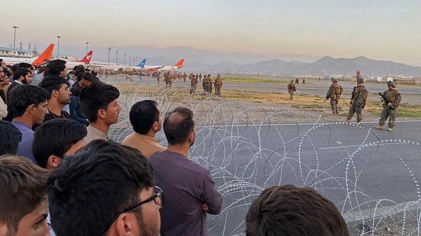 Afghans (L) crowd at the airport as US soldiers stand guard in Kabul on August 16, 2021. (Photo by Shakib Rahmani / AFP)