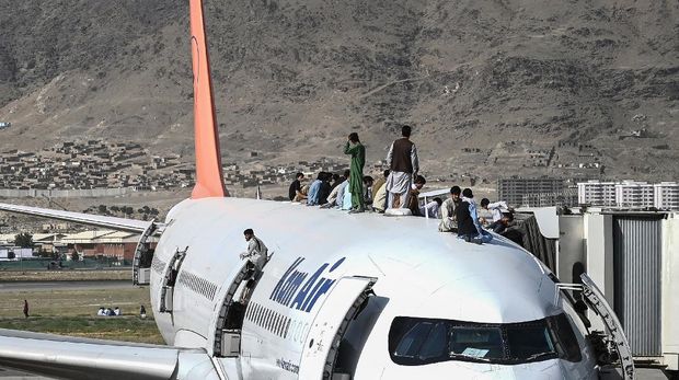 Afghan people climb atop a plane as they wait at the Kabul airport in Kabul on August 16, 2021, after a stunningly swift end to Afghanistan's 20-year war, as thousands of people mobbed the city's airport trying to flee the group's feared hardline brand of Islamist rule. (Photo by Wakil Kohsar / AFP)