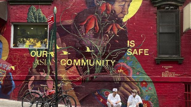 Two chefs rest against a mural during their cigarette break in the Chinatown area of Manhattan on Monday, Aug. 9, 2021, in New York. (AP Photo/Wong Maye-E)