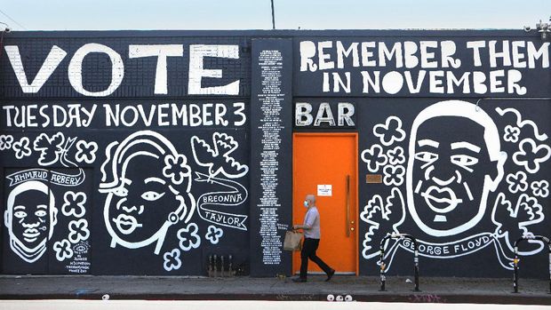 Kritik Lewat Mural, Tembok-tembok yang Melawan LOS ANGELES, CALIFORNIA - OCTOBER 02: A man walks past a mural by artist Eric Junker which reads Vote- Remember Them In November on October 2, 2020 in Los Angeles, California. The mural features images of deceased Black shooting victims George Floyd, Breonna Taylor and Ahmaud Arbery. Floyd and Taylor were killed by police while Arbery was gunned down by two white men in Georgia while jogging. President Donald Trump and Democratic presidential nominee Joe Biden are on the ballot for the 2020 presidential elections on November 3. Mario Tama/Getty Images/AFP (Photo by MARIO TAMA / GETTY IMAGES NORTH AMERICA / Getty Images via AFP)