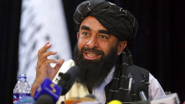 In front of a Taliban flag, Taliban spokesman Zabihullah Mujahid speaks at at his first news conference, in Kabul, Afghanistan, Tuesday, Aug. 17, 2021. For years, Mujahid had been a shadowy figure issuing statements on behalf of the militants. Mujahid vowed Tuesday that the Taliban would respect women's rights, forgive those who resisted them and ensure a secure Afghanistan as part of a publicity blitz aimed at convincing world powers and a fearful population that they have changed. (AP Photo/Rahmat Gul)