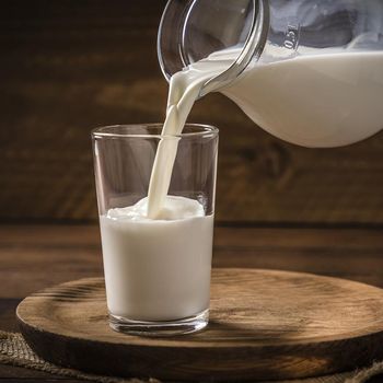 Front view of a pitcher pouring milk into a drinking glass on a rustic wooden background. Low key DSLR photo taken with Canon EOS 6D Mark II and Canon EF 24-105 mm f/4L