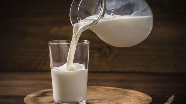 Front view of a pitcher pouring milk into a drinking glass on a rustic wooden background. Low key DSLR photo taken with Canon EOS 6D Mark II and Canon EF 24-105 mm f/4L