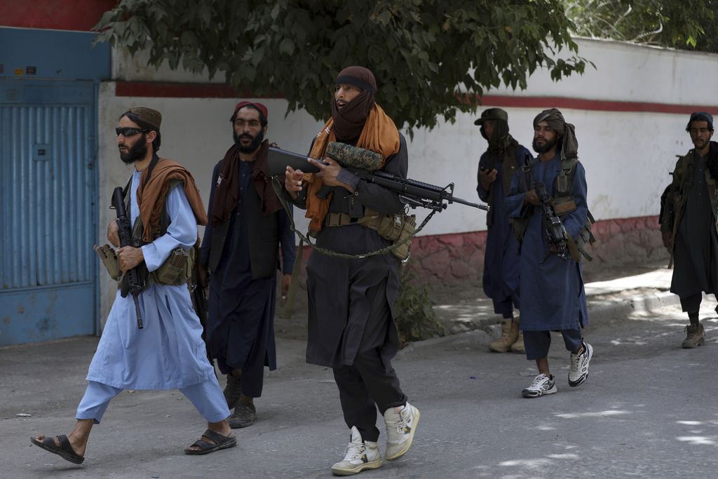 Taliban fighters patrol as two Traffic policemen stand, left, in Kabul, Afghanistan, Thursday, Aug. 19, 2021. The Taliban celebrated Afghanistan's Independence Day on Thursday by declaring they beat the United States, but challenges to their rule ranging from running a country severely short on cash and bureaucrats to potentially facing an armed opposition began to emerge. (AP Photo/Rahmat Gul)