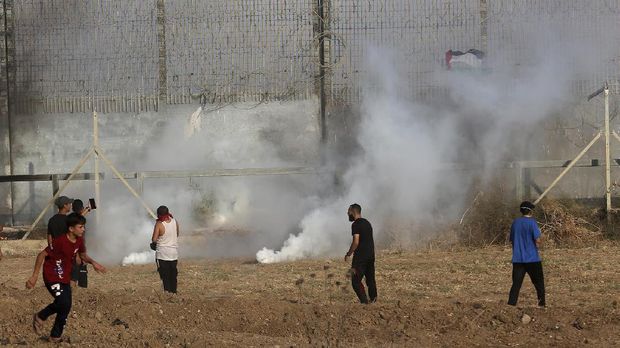 Israel Tembaki Demonstran Palestina di Gaza Protestors run to cover from teargas fired by Israeli troops near fence of Gaza Strip border with Israel, during a protest marking the anniversary of a 1969 arson attack at Jerusalem's Al-Aqsa mosque by an Australian tourist later found to be mentally ill, east of Gaza City, Saturday, Aug. 21, 2021. (AP Photo/Adel Hana)