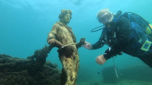 In this photograph taken on August 18, 2021 a dive guide shows tourists a copy of the original statues preserved at the Museum of Baiae, representing Dionysus with ivy crown in the Nymphaeum of punta Epitaffio, the submerged ancient Roman city of Baiae at the Baiae Underwater Park, part of the Campi Flegrei Archaeological Park complex site in Pozzuoli near Naples. - Statues which once decorated luxury abodes in this beachside resort are now playgrounds for crabs off the coast of Italy, where divers can explore ruins of palaces and domed bathhouses built for emperors. (Photo by Andreas SOLARO / AFP)
