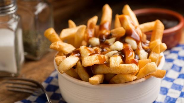 camilan poutine Classic French Canadian poutine with french fries, gravy, and cheese curds on a rustic tabletop.