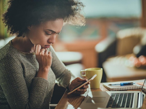 Young black woman reading a problematic text message on her mobile phone while working at home.