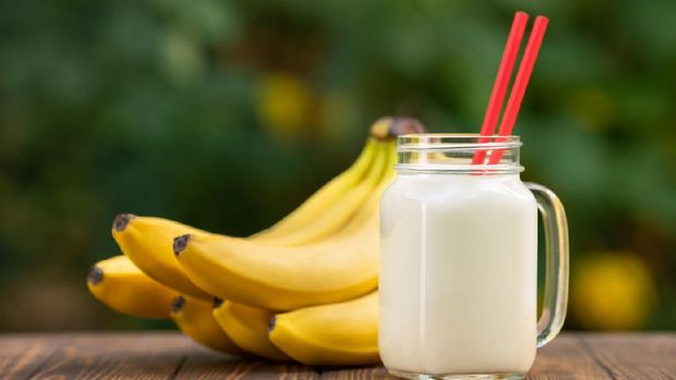banana smoothie in mason jar on wooden table with green blurred natural background