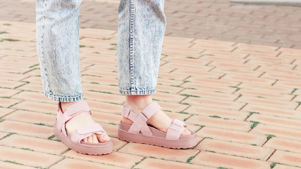 Female feet in a pink sandals on concrete background close-up.