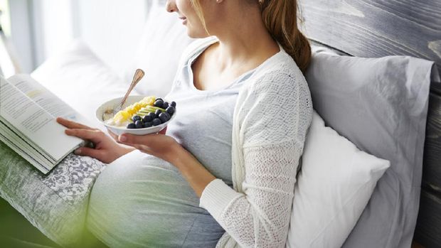Young mother eating and reading book at home
