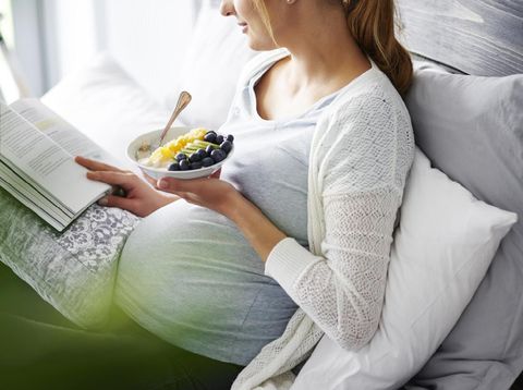 Young mother eating and reading book at home