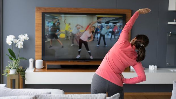 Back view of senior woman following an online stretching class looking at TV screen - Technology concepts. **IMAGE ON SCREEN BELONGS TO US**