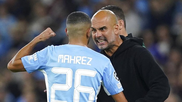 Manchester Citys Riyad Mahrez speaks with manager Pep Guardiola on the touchline during the Champions League Group A soccer match between Manchester City and RB Leipzig at the Etihad Stadium, Manchester, England, Wednesday Sept. 15, 2021. (Martin Rickett/PA via AP)