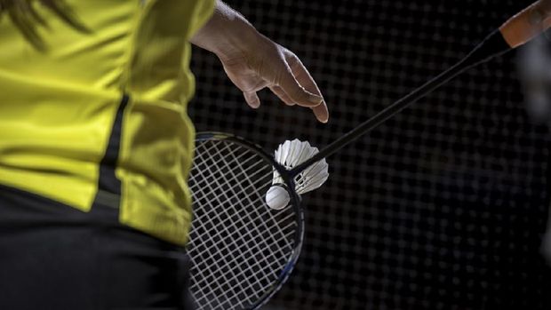 Woman holding a bulu tangkis racket and dropping a shuttlecock about to serve.