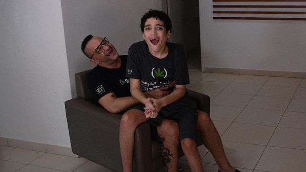 Gabriel Guerra (R) is seen with his father, Ricardo Guerra, in Rio de Janeiro, Brazil, on September 20, 2021. - Ricardo gives his son medicinal cannabis in the form of droplets to help his severe autism and cerebral palsy. His son was told at an early age that he would never be able to be mobile but the medicine has stopped his seizures and allowed him to walk. (Photo by Carl de Souza / AFP)