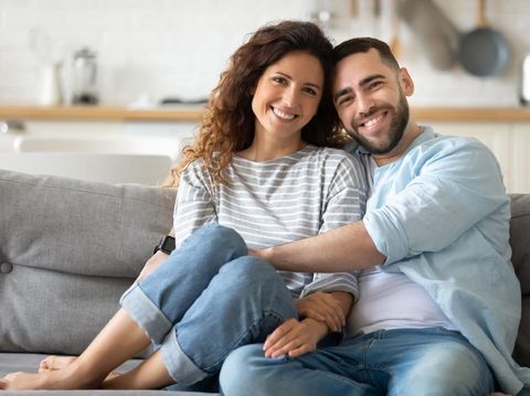Portrait of young 35s just married couple in love posing photo shooting seated on couch in modern studio apartments, concept of capture happy moment, harmonic relationships, care and sincere feelings