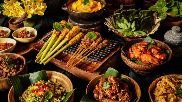 An assortment of Balinese dishes to accompany the steamed rice (not shown). The dishes are Sate Lilit (minced meat satay) and Sate Babi (pork satay), Gedang Mekuah (green papaya soup), Tum Ayam (minced chicken parcel), Udang Goreng (pan-fried prawns), Rempeyek (peanut crackers), Ayam Klungkung (chicken with crushed chili pepper), Lawar Ayam (long bean and chicken salad), Babi Goreng (seasoned pork crisps), and three chili condiments of Sambal Plecing (red chili sauce), Sambal Embe (fried red chili and shallots), Sambal Matah (shallots and lemongrass salsa). A bouquet of Frangipani is used as table decoration.