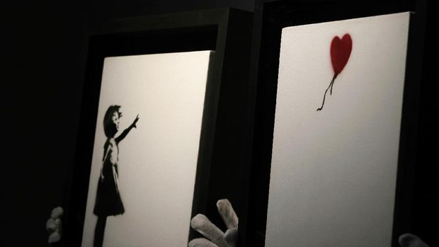 Members of staff hold up an artwork by British graffiti artist Banksy entitled 'Girl and Ballon' (two parts), during a pre-auction press viewing at Christie's auction house in London, Friday, Oct. 1, 2021. The diptych is expected to sell for 2,500,000 million pounds sterling (US, $3.5-4.8 million, euros 3-4.1 million). (AP Photo/Alastair Grant)