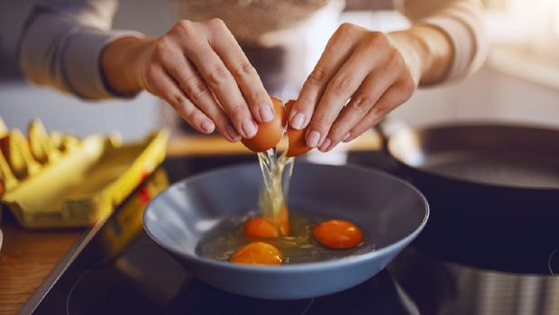 Close up of caucasian woman breaking egg and making sunny side up eggs. Domestic kitchen interior. Breakfast preparation.