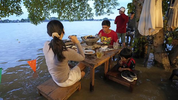 Customers of the riverside Chaopraya Antique Café enjoy themselves despite the extraordinary high water levels in the Chao Phraya River in Nonthaburi, near Bangkok, Thailand, Thursday, Oct. 7, 2021. The flood-hit restaurant has become an unlikely dining hotspot after fun-loving foodies began flocking to its water-logged deck to eat amid the lapping tide. Now, instead of empty chairs and vacant tables the “Chaopraya Antique Café” is as full as ever, offering an experience the canny owner has re-branded as “hot-pot surfing.” (AP Photo/Sakchai Lalit)