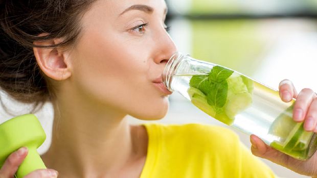 Close-up of a woman drinking water with mint, cucumber and lime during a workout with dumbbells. Detox dieting concept