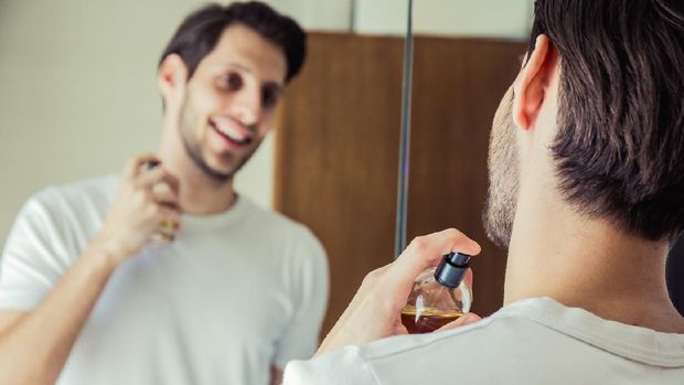 man puts perfume in the bathroom in front of the mirror